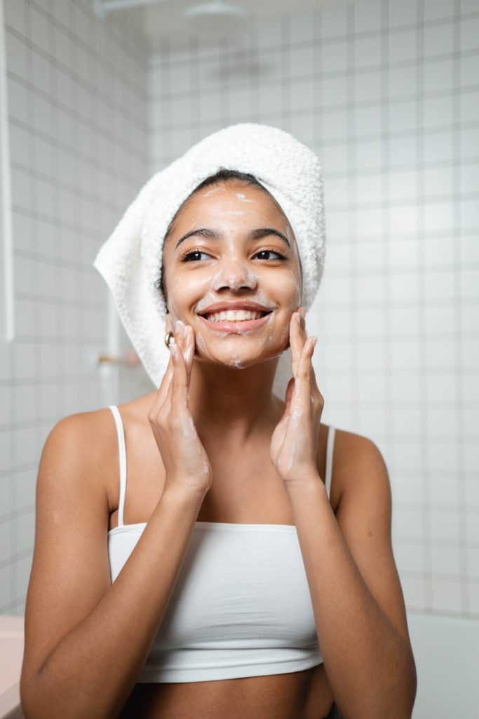 woman with hair wrapped in towel performing skin care routine